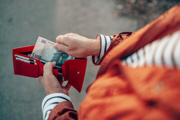 Female takes out 5 euro banknote from a red leather wallet on the street - obrazy, fototapety, plakaty