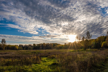 Fototapeta na wymiar The sun's rays from under a large dark cloud fall on an autumn field with dry grass.