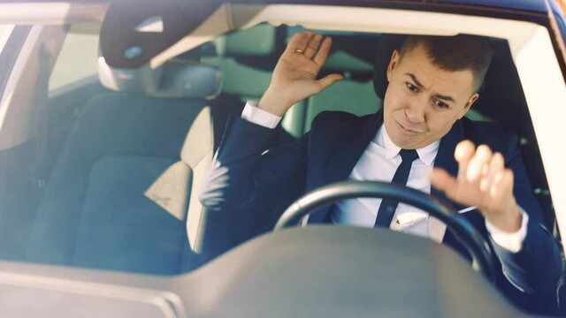 Angry man sitting in car and pounding with hands on steering wheel. Unhappy young man driving sitting car in city at sunlight. Feel angry stress depression. Look serious automobile. Frustrated tired.