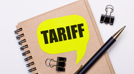 On a light background, a brown notebook, a black pen and paper clips, and a yellow card with the text TARIFF. Business concept.
