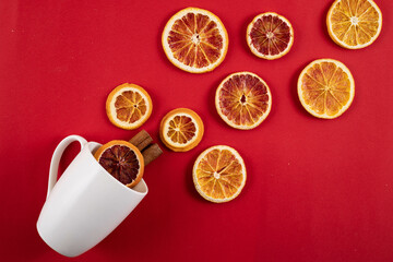 White mug with scattered dried orange slices and cinnamon on a red background.