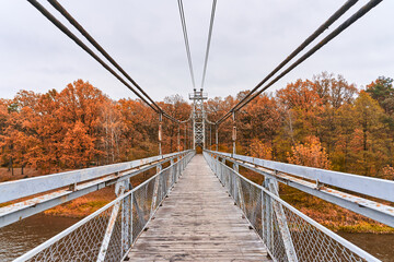 The long suspension bridge goes into the distance. Autumn yellow forest stands on the background. Place for walking
