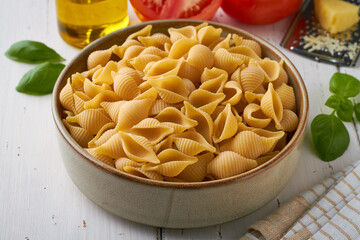 italian pasta conchiglie rigate in a plate with basil tomato olive oil pepper parmesan cheese on white background