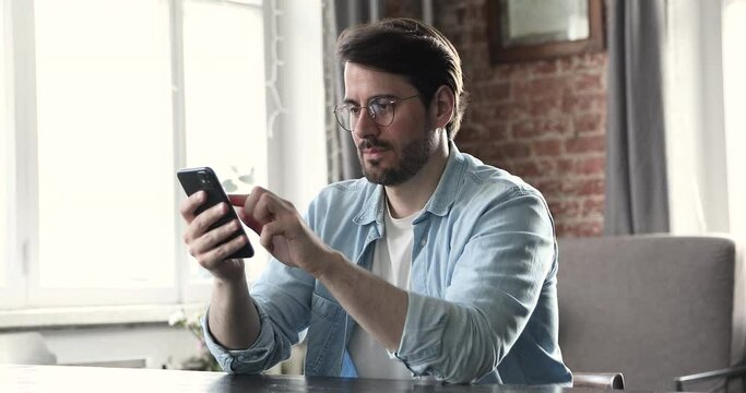 Man sit at table holds smartphone feels angry dissatisfied by discharged or broken device, problems with gadget. Annoyed guy receive message read sms with bad news. Malfunction, need repair concept