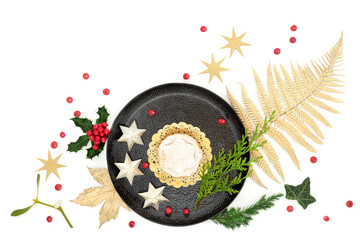 Luxury Christmas mince pie treat on plate with gold leaf, star tree decorations, holly, loose berries and winter flora on white background. Festive food nature composition for the holiday season.  