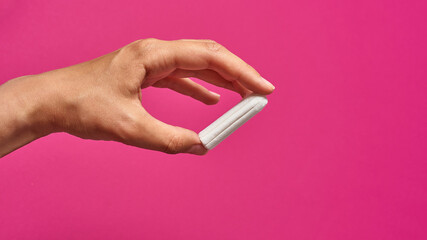 hygienic tampon in a female hand on a pink background