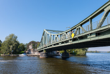 The famous historical Glienicke Bridge between Berlin and Potsdam photographed from a boat. It's a summer day with blue skies. There is a small motorboat at the landing stage.