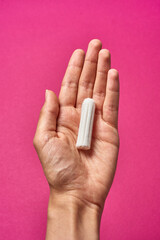 hygienic tampon in a female hand on a pink background