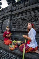 Two young girls in traditional clothing are preparing offerings. Hindu Balinese temple, Bali, Indonesia.