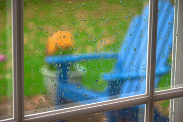 Blue Adirondack chairs sit on a patio in Autumn in Hershey PA.  Looking through a window during a heavy rain wishing it was sunny so you could sit outside.