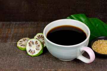 Noni juice in ceramic cup and fresh noni fruit with green leaf on rustic wooden background.