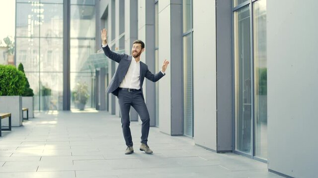 Cheerful happy business man dancing walk the city ​​street background a modern office building outside, outdoors Funny successful businessman in suit rejoices joyfully jump celebrates victory, success