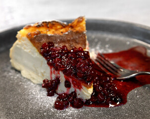 A slice of cheesecake with cranberry sauce on a large gray plate with a fork next to it. close-up view. High quality photo