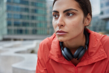 Close up shot of thoughtful athletic young woman takes break after intensive cardio workout wears...