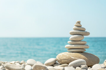 Balanced stack of pebbles on sea beach on sunny day. Natural summer harmony concept with stone pyramid on the coast.