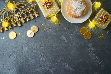 Jewish holiday Hanukkah concept with traditional donuts, menorah and gift box on dark background. Top view with copy space
