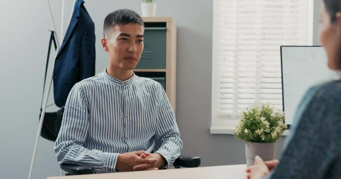 Disabled man dressed in smart blue striped shirt sits at desk in corporate office in wheelchair, he is applying for secretarial job, female corporate executive is conducting interview she ask question