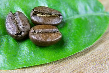 Roasted coffee beans on wooden background. Green leaves and scattered coffee beans.