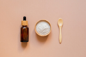 Dry clay for face mask in a wooden bowl with a spoon and amber glass dropper bottle. Top view on beige background. Skincare natural cosmetic.