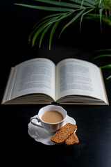 Reading a book with a  cup of coffee and two little biscuits