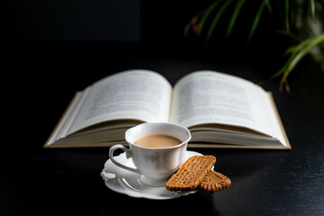 Reading a book with a  cup of coffee and two little biscuits