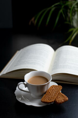 Reading a book with a  cup of coffee and two little biscuits