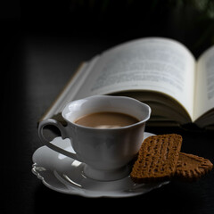 Reading a book with a  cup of coffee and two little biscuits
