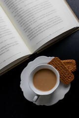 Reading a book with a  cup of coffee and two little biscuits