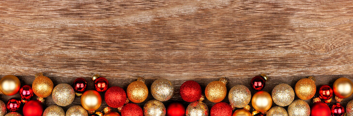 Christmas bottom border of red and gold decorations. Top view on a rustic wood banner background. Copy space.