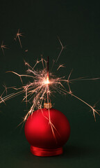 Christmas red ball and Sparkler lights on dark green background. Concept: Christmas and New Year, Invitation, Greeting card. Christmas background. Vertical