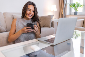 Using her laptop and bluetooth earbuds, the mid adult woman video conferences from home during the...