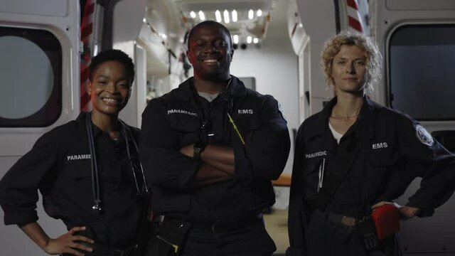 Multi ethnic paramedics smiling on camera near ambulance