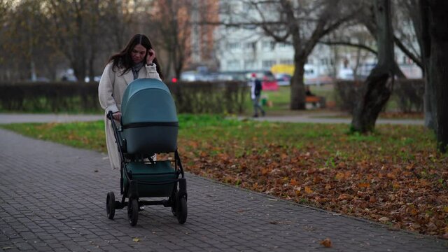 Mother with baby stroller on a walk in the park in autumn