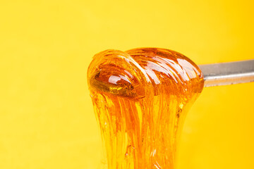 amber yellow cannabis wax concentrate dripping from the dabbing tool close-up - obrazy, fototapety, plakaty