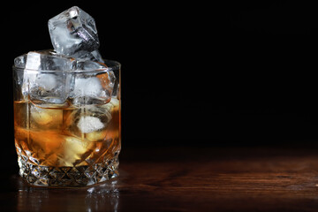 A glass of strong alcoholic drink with ice on a wooden bar counter. Whiskey with ice cubes. Glass with a chilled drink.