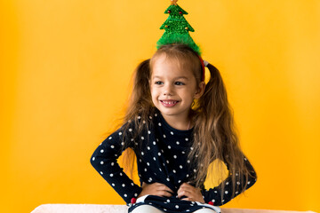 Portrait of positive smiling surprised happy little schoolgirl girl Christmas tree decoration on head polka dot dress show thumbs up orange background. New year, holiday, celebration, winter concept