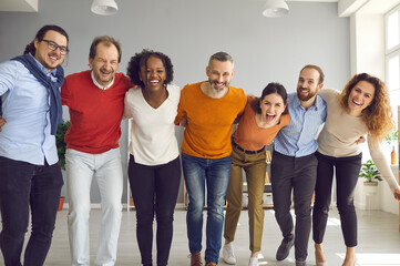 Team of business colleagues and friends having fun together. Group portrait of happy diverse people standing in row, huddling, laughing and looking at camera. Support, union and friendship concept
