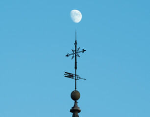 Fototapeta na wymiar Cross on top of a church pointing to the moon on blue sky.