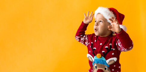 Portrait of happy smiling positive joyful positive preschool little boy in red warm santa hat showing thumb up on orange, yellow background. Winter, holiday, celebration, Christmas, New Year copy