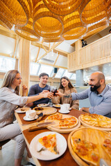 A group of young cheerful friends is sitting in a cafe talking and eating pizza. Lunch at the pizzeria.