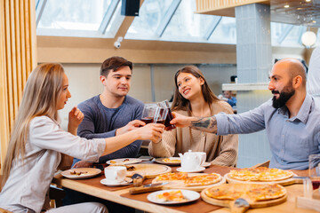 A group of young cheerful friends is sitting in a cafe talking and eating pizza. Lunch at the pizzeria.