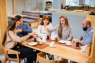 A group of young cheerful friends is sitting in a cafe talking and eating pizza. Lunch at the pizzeria.