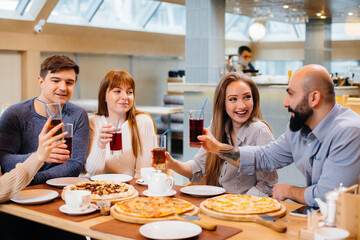 A group of young cheerful friends is sitting in a cafe talking and eating pizza. Lunch at the pizzeria.