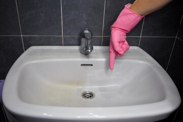 A half-washed bathroom sink, a woman's hand in a pink glove points to the clean half