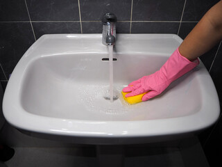 Woman doing chores in the bathroom at home, washing the sink and tap with detergent and water