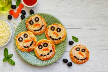 Mini snowman pizzas made it from pizza crust,pizza sauce,mozzarella cheeses,black olives and carrots on plate with white wood background.Art food idea for kids Christmas party.Top view.Copy space