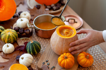 Young woman in apron preparing delicious homemade pumpkin soup on her kitchen. Fresh organic ingredients, traditional autumn food. Healthy eating, cozy home atmosphere