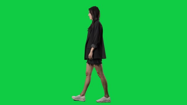 Side view of stylish smart casual woman in suit jacket and skirt walking. Full body isolated on green screen background