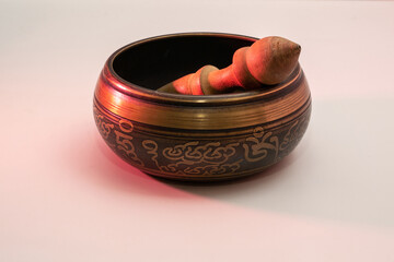 Photo of tibetan singing metal bowl for meditation with ringing stick deep inside on white background lit with red light 