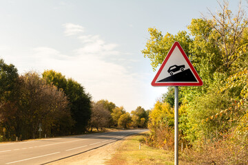 Triangular road sign steep climb against the background of autumn trees near the track